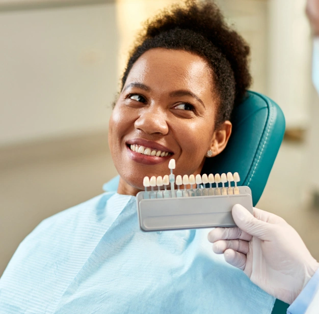Smiling dental professional holding tooth shade guide in dental office setting.