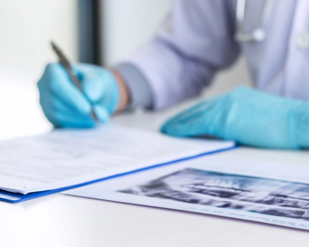 Dentist in blue gloves examining dental X-rays at white desk in clinical setting.