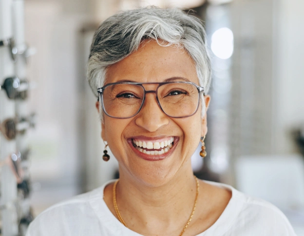 Smiling woman with gray hair and glasses in a dental office setting.