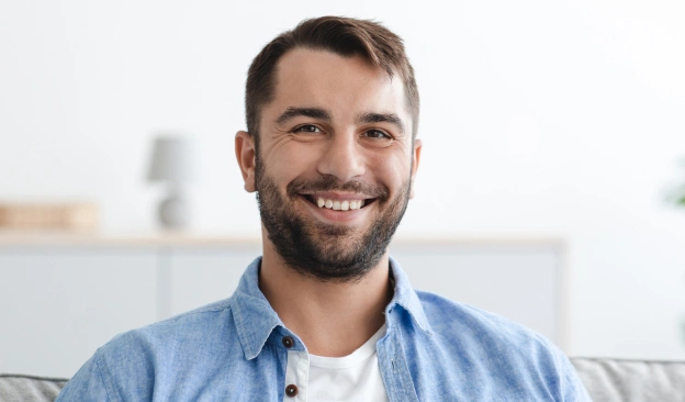 Smiling male dentist in blue shirt and white undershirt in modern dental office setting.