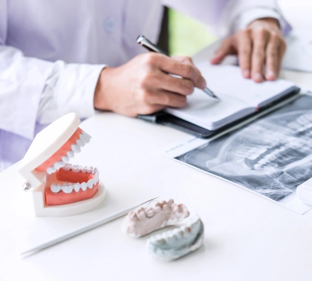 Dentist reviewing dental x-rays and models at desk with patient records and dental models.