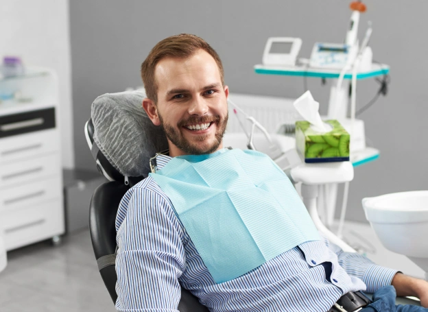 Smiling male patient in dental chair wearing bib at modern dental office