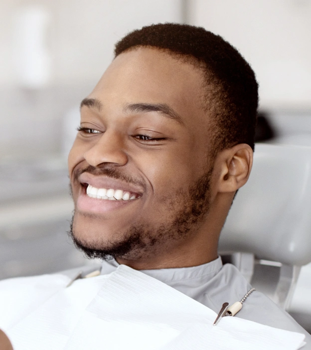 Smiling man in white shirt in bright dental office setting, appearing happy and relaxed.