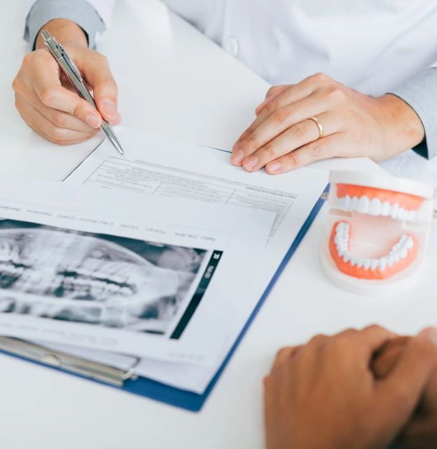 Dentist examining X-ray with patient, dental model and tools on desk.