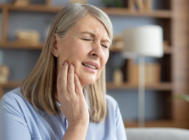 Woman experiencing tooth pain, holding jaw with hand in home setting.