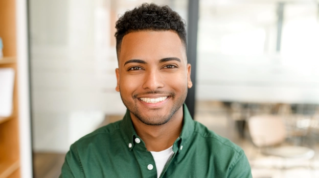 Smiling male dental professional wearing green shirt in modern dental office setting.