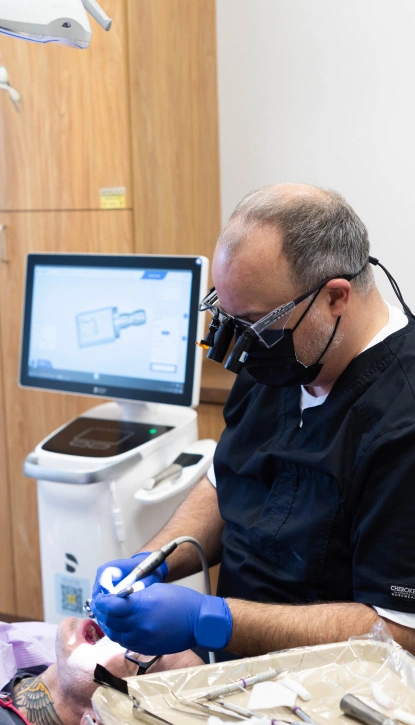 Dentist in blue gloves examining patient sample at computer workstation in dental office.