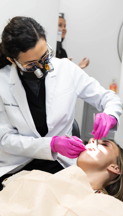 Dentist in white coat and pink gloves examining patient's teeth in dental office.