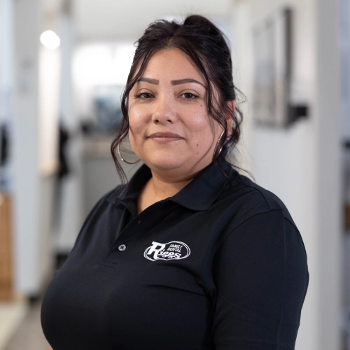 Woman in black polo shirt with dental practice logo standing in modern dental office hallway.