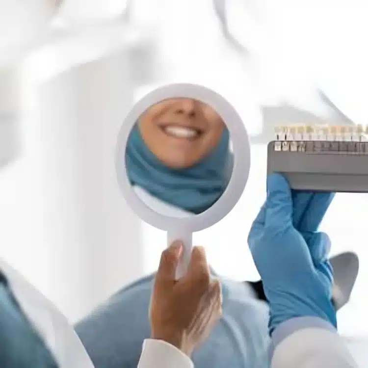 Dental professional in blue scrubs holding mirror showing patient's smile during examination.