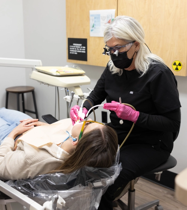 Dental professional wearing mask examines patient in dental office treatment room.