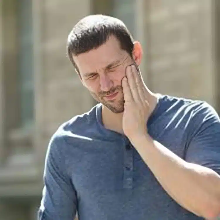 Man in blue shirt touching face with hand, smiling outdoors near building.