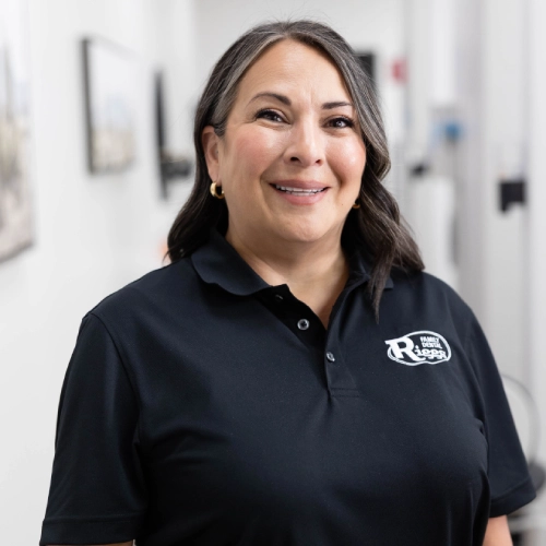 Woman in black Riggs Family Dental polo shirt smiling in bright dental office setting.