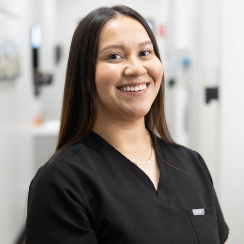 Smiling dental professional in black scrubs in a modern clinical setting.
