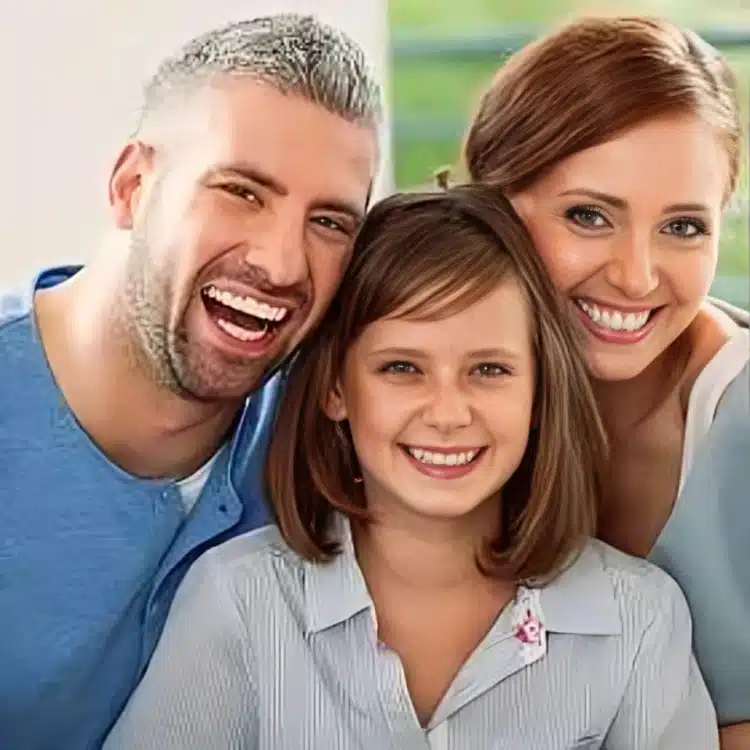 Happy family of three smiling together in casual indoor portrait for dental practice.