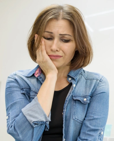 Woman in denim shirt touching face, looking thoughtful against white background.