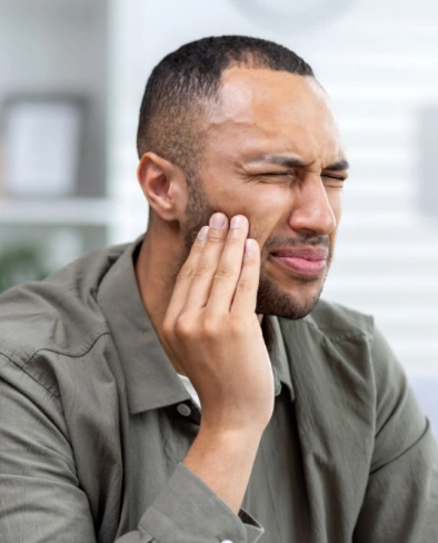 Man experiencing tooth pain, holding cheek, in dental office setting.