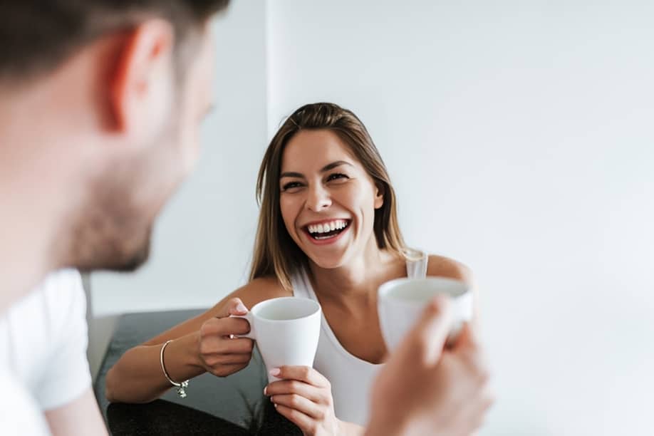 Two people sharing coffee and smiling in a bright, modern dental office setting.