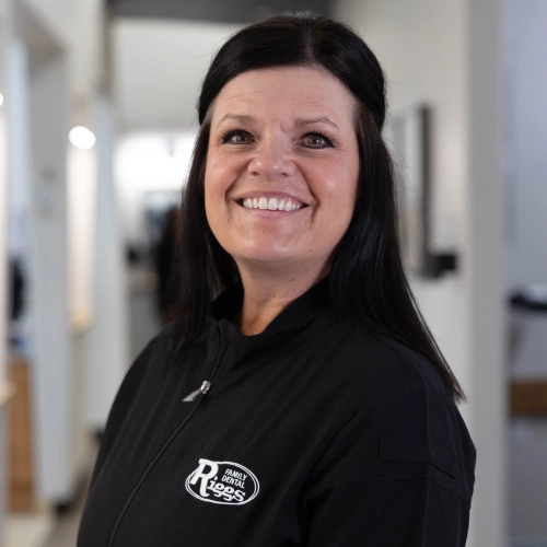 Professional woman smiling at dental office, wearing black Riggs Family Dental branded shirt.