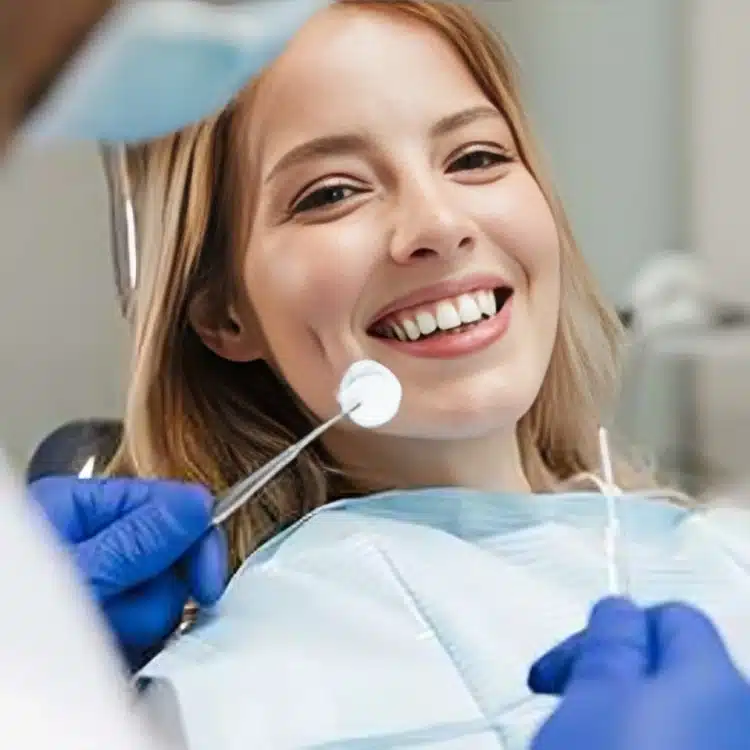 Young patient smiling during dental examination with dentist using mirror and tools in dental office.