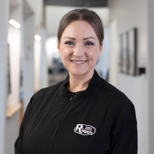 Professional dental staff member smiling in modern clinic hallway wearing Riggs Family Dental branded jacket