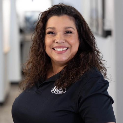 Woman smiling at camera wearing dark Riggs Family Dental polo shirt in clinical office setting.