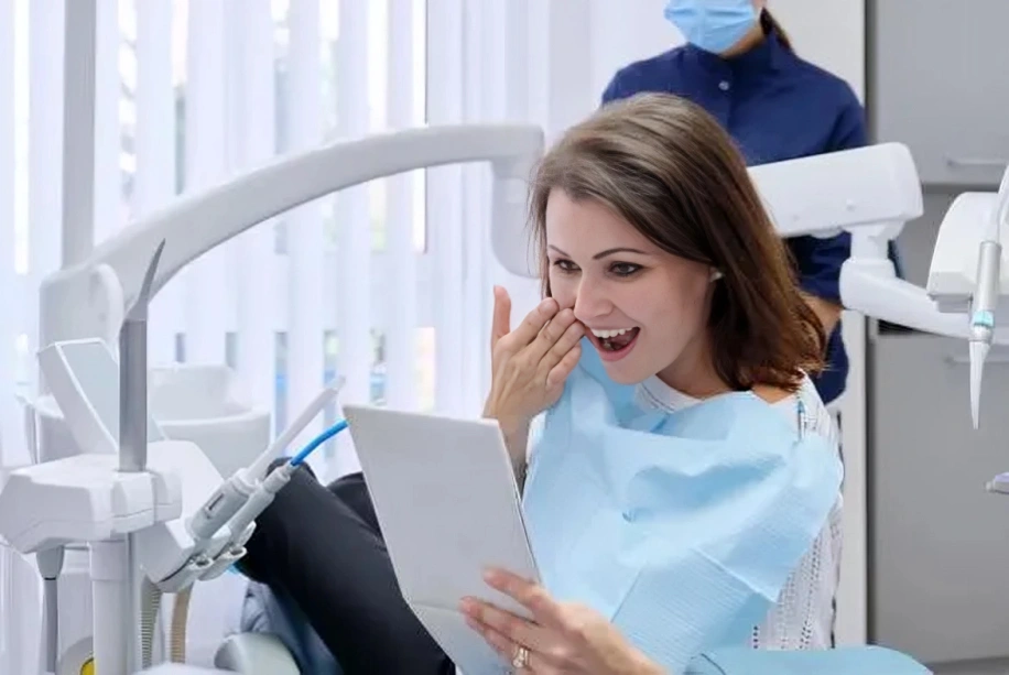Patient in dental bib smiling while holding mirror in dentist's office chair.