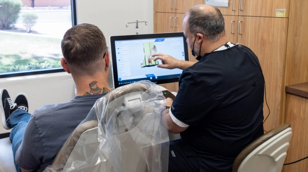 Dentist and assistant conducting virtual consultation with patient on laptop in dental office.