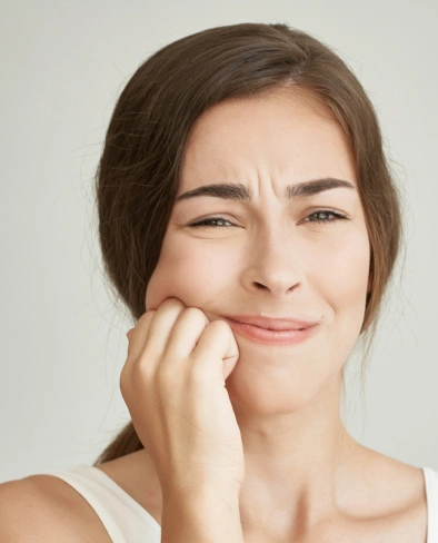 Woman with hand to face displaying thoughtful expression against neutral background.