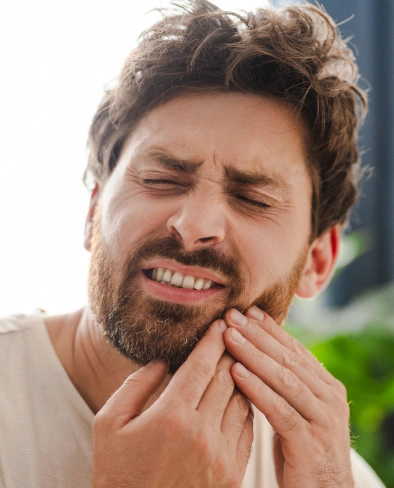 Man with beard touching cheek in pain, suggesting toothache or dental discomfort outdoors.