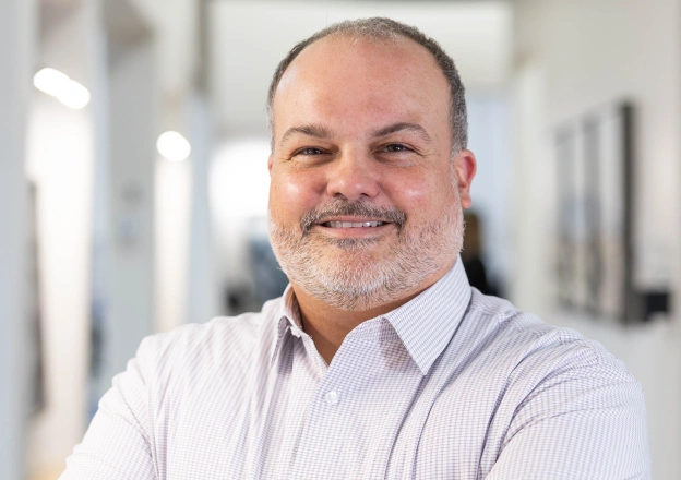 Middle-aged man in light blue shirt smiling at camera in bright dental office setting.