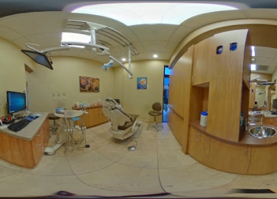 Modern dental office interior with treatment chairs, equipment, and reception area in warm tones.
