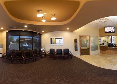 Modern dental office waiting room with seating, curved reception desk, and contemporary lighting fixtures.