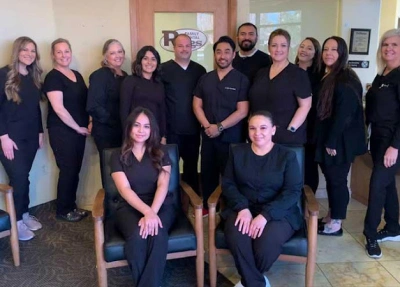 Large dental team in black scrubs posing together indoors at Riggs Family Dental office.