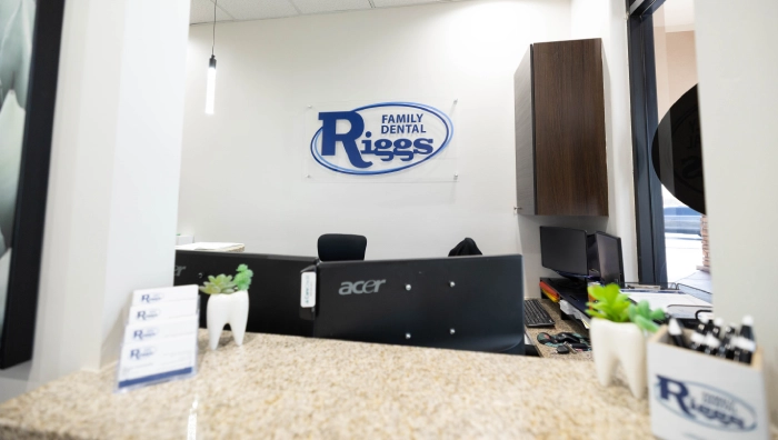 Riggs Family Dental reception desk with logo on wall, computer equipment, and waiting area.