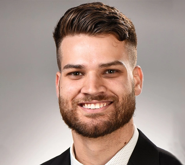 Professional headshot of smiling man in black jacket against neutral gray background.